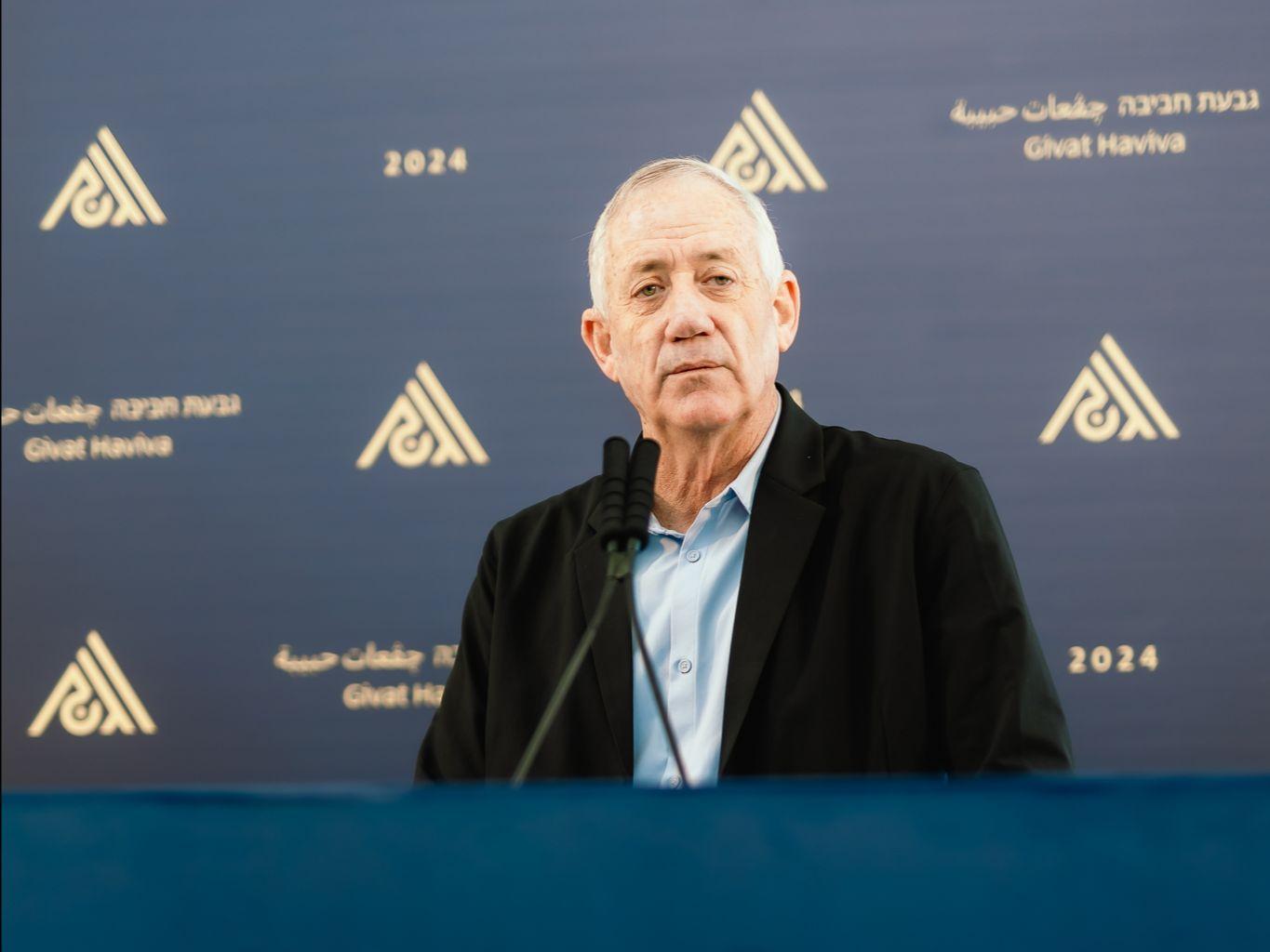 A man with white hair stands behind a podium at a conference